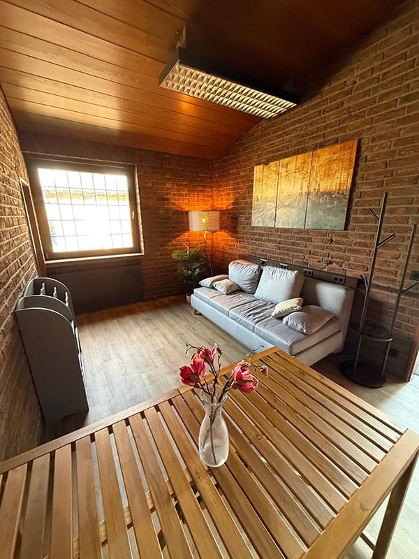 Der Nebenraum mit Sofa, großem Holztisch und Backsteinwänden